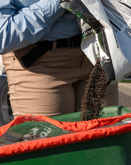 Technician pouring fertilizer into spreader