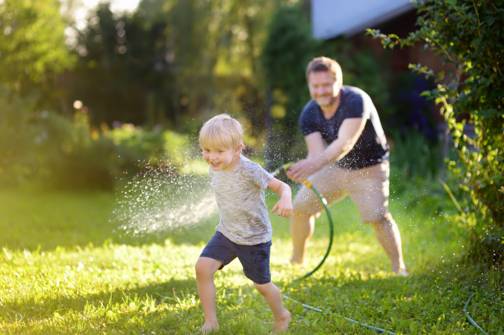 Father and son playing with a garden hose on a healthy green lawn